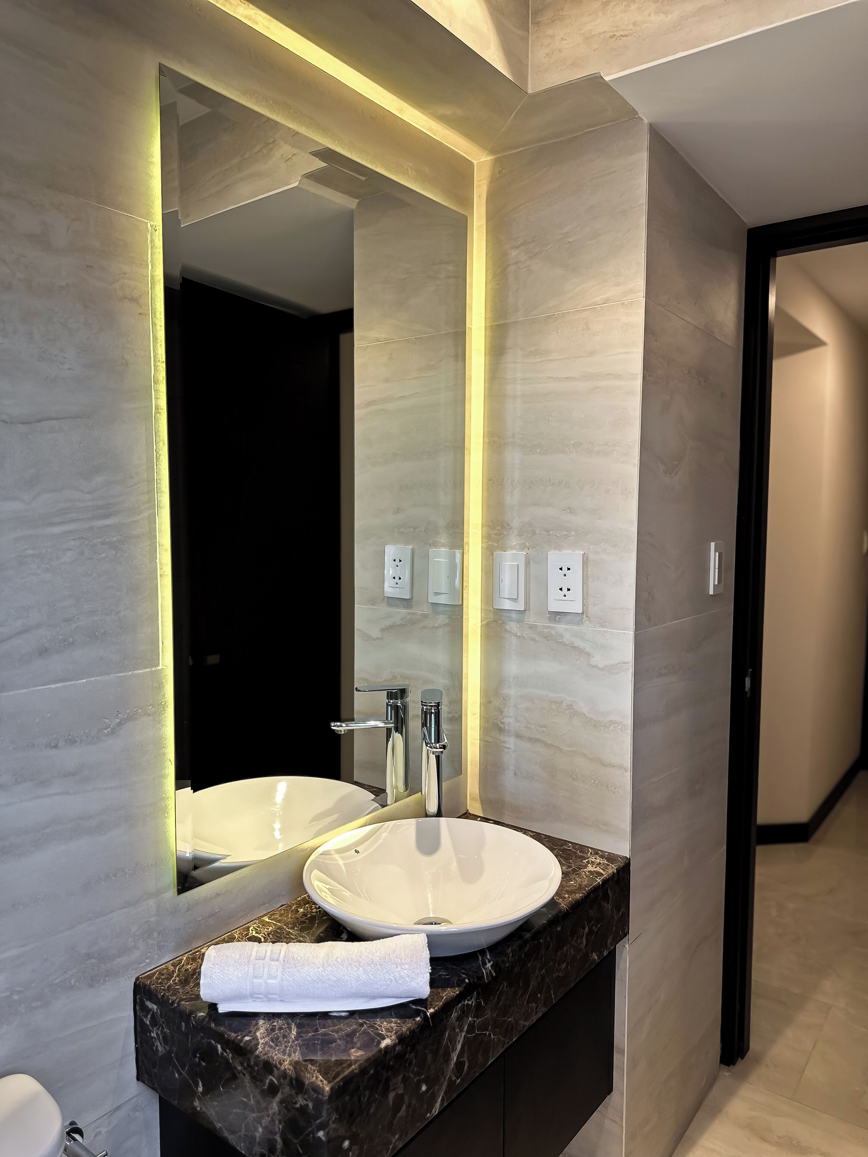 A modern bathroom with a large mirror, a white sink, and a marble countertop.