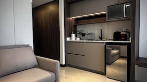 A modern living room with a sofa and a kitchen area featuring a microwave, kettle, and a coffee machine. - AMERICA APARTMENTS (Santa Cruz)