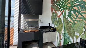A modern kitchen with a built-in grill, a black countertop, and a wall mural of tropical leaves. - AMERICA APARTMENTS (Santa Cruz)