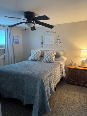 A bedroom with a bed, a ceiling fan, a nightstand with a lamp, and wall decorations including an anchor and a fish. - updated, lakefront 4-bedroom house with AC in Ashville on Chautauqua Lake (Ashville)