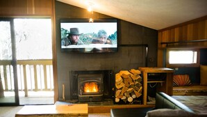 Una sala de estar acogedora con chimenea, un televisor montado en la pared y una pila de leña.