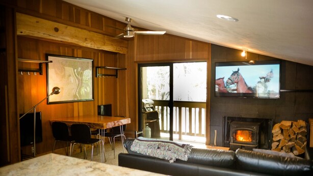 Una sala de estar acogedora con chimenea, un televisor montado en la pared, techo de madera y un ventanal grande.