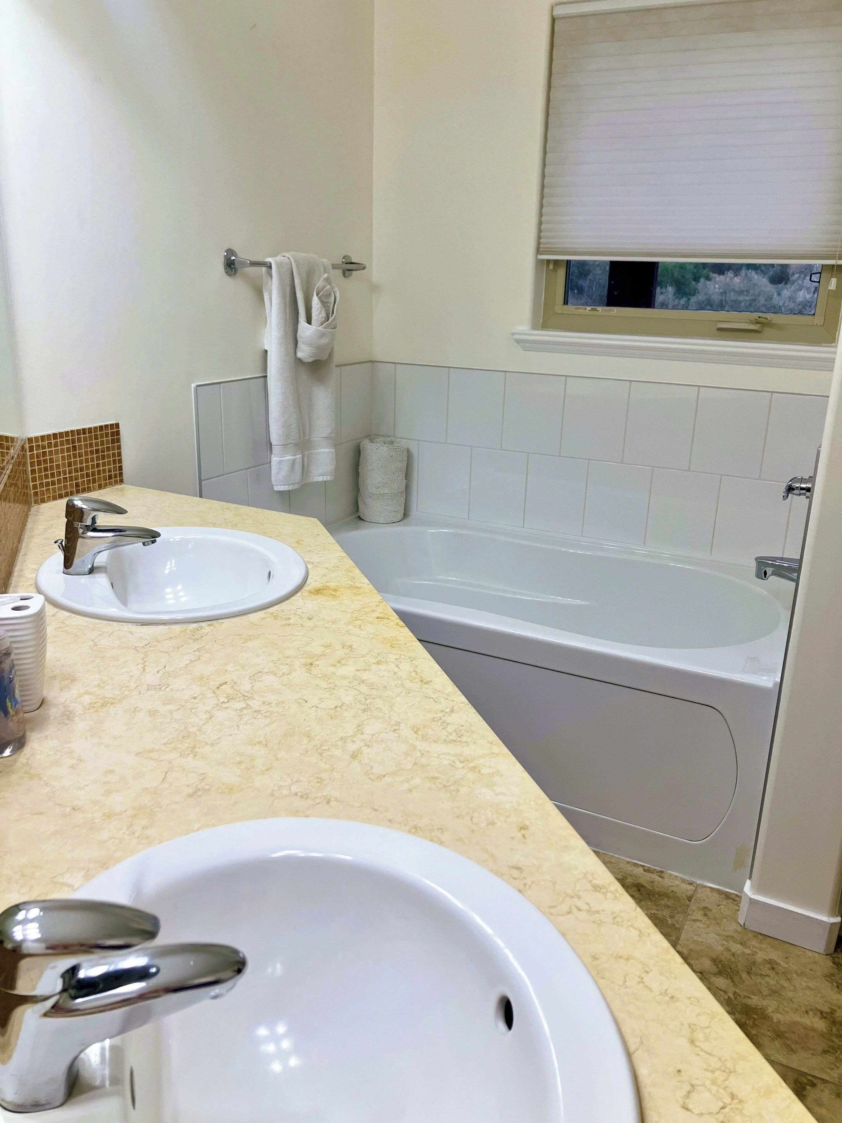 A bathroom with two sinks, a bathtub, and a window with a view of trees.