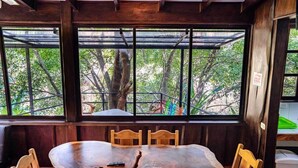 Una mesa de comedor de madera con sillas, ventanas amplias con vista a árboles y una barandilla de metal.