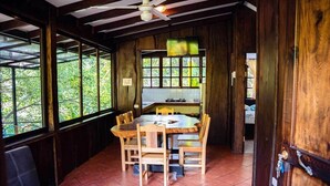 Un comedor de madera con una mesa redonda y sillas, un ventilador de techo y ventanas grandes.