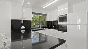 Una cocina moderna con armarios blancos, encimera negra y electrodomésticos integrados, incluyendo un microondas, horno y refrigerador.