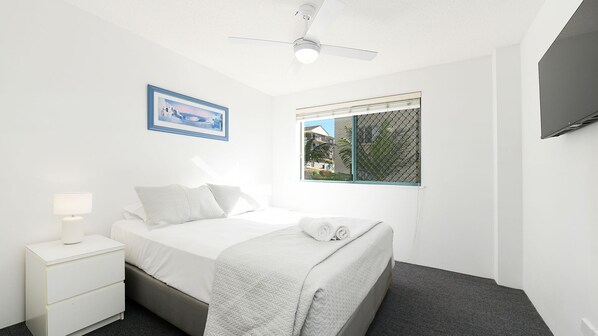A bedroom with a bed, a nightstand, a ceiling fan, a window with a view, and a framed picture on the wall. - Lindomare Unit 6, 11 Orvieto Tce, Kings Beach (Kings Beach)
