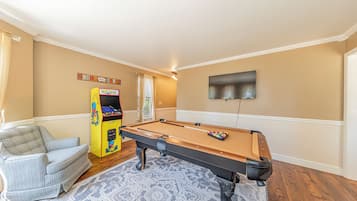 A pool table in a room with a sofa and a Pac-Man arcade machine.