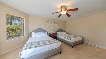 A bedroom with two beds, a ceiling fan, a window with blinds, and a wall-mounted macrame decoration.