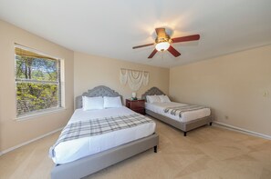 A bedroom with two beds, a ceiling fan, a window with blinds, and a wall-mounted macrame decoration.