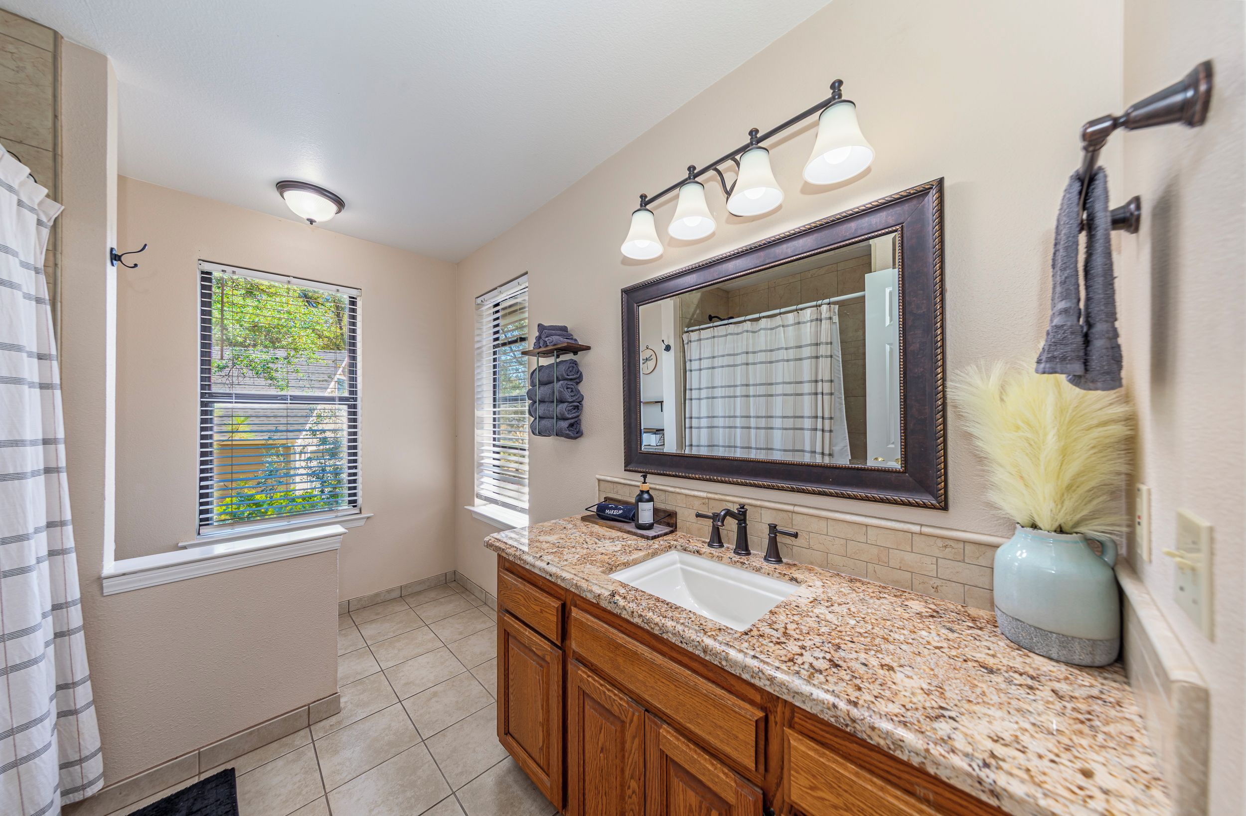 A bathroom with a vanity, sink, mirror, towel rack, and a window with blinds.