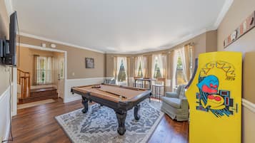 A pool table in a room with a patterned rug, a sofa, and a yellow board with a cartoon character.