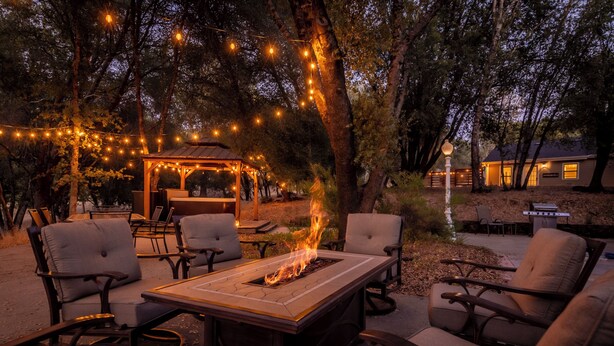 An outdoor seating area with a fire feature, surrounded by trees and string lights.