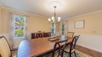 A dining room with a large wooden table, six chairs, a chandelier, and a framed quote on the wall.