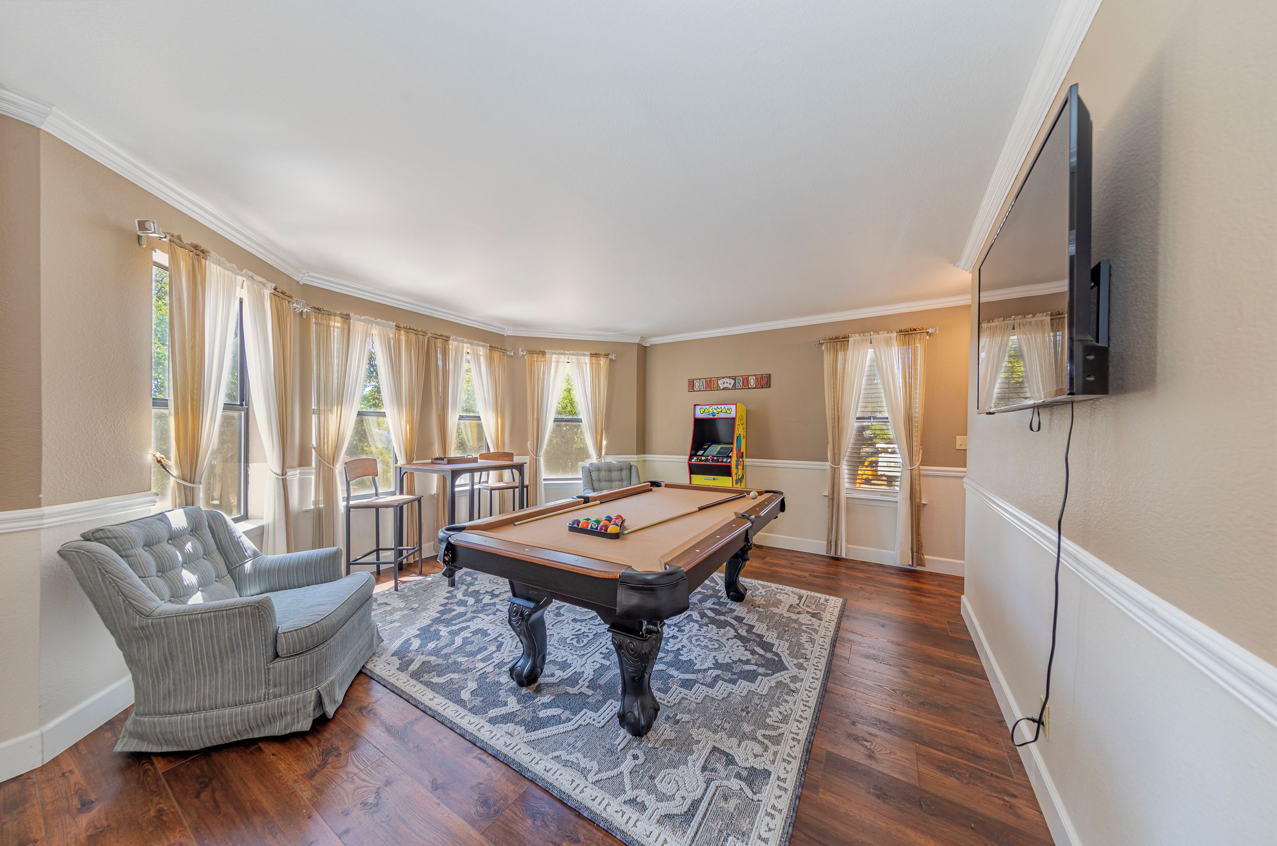 A pool table in a room with a sofa, a television, and a pinball machine.
