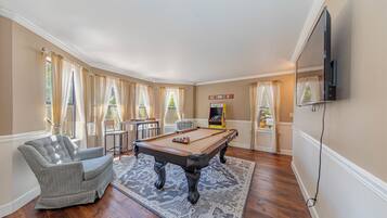 A pool table in a room with a sofa, a television, and a pinball machine.