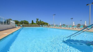 A clear blue pool with white poolside chairs and umbrellas, surrounded by a white fence and palm trees. - Cozy apartment in Prunete with swimming pool (Prunete)