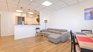 A modern living room with a grey sectional sofa, a wooden dining table, and a small kitchen area with a refrigerator and a sink. - Cozy apartment in Prunete with swimming pool (Prunete)