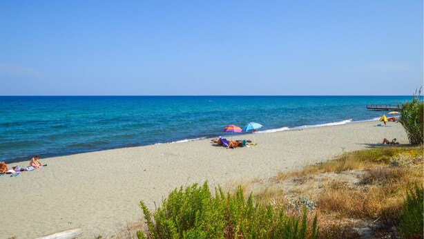 A beach with clear blue water, a sandy shore, and a few umbrellas. - Cozy apartment in Prunete with swimming pool (Prunete)