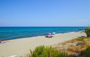 Une plage à l’eau d’un bleu limpide, avec un rivage sablonneux et quelques parasols.