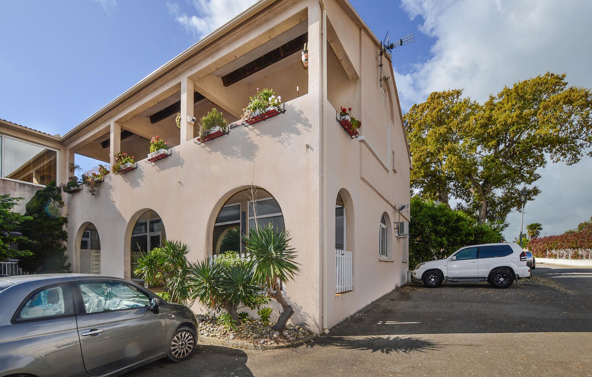 A building with arched windows and a flat roof, featuring outdoor planters with flowers.