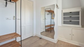 Una stanza con una panca in legno, un armadio bianco con cassetti e uno specchio che riflette un appendiabiti.