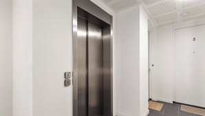 En moderne elevator med metalfinish, en hvid væg og et flisegulv.