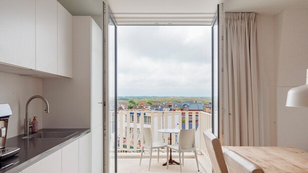 Et moderne køkken med indbygget kaffemaskine, vask og udsigt til en balkon med et bord og stole.