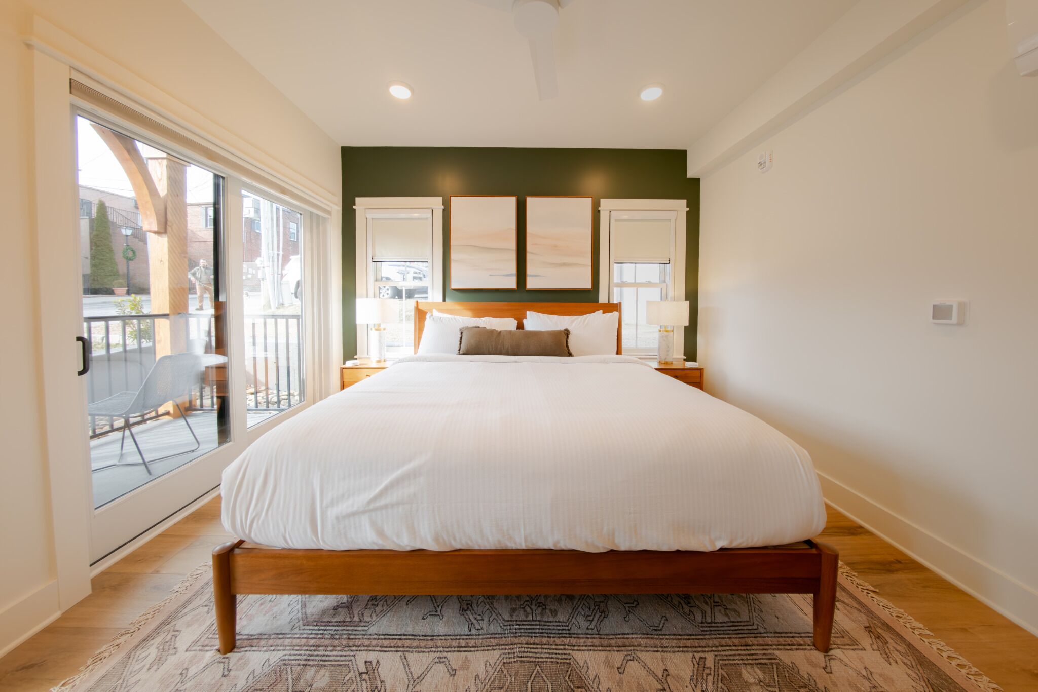 A bedroom with a large bed, a view through a sliding glass door, and a green accent wall.