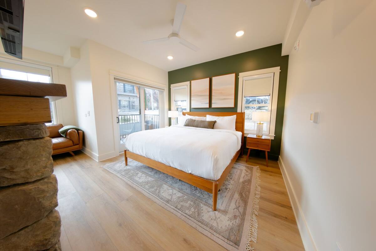 Un dormitorio con cama, mesita de noche, lámpara, ventilador de techo y vistas al exterior.