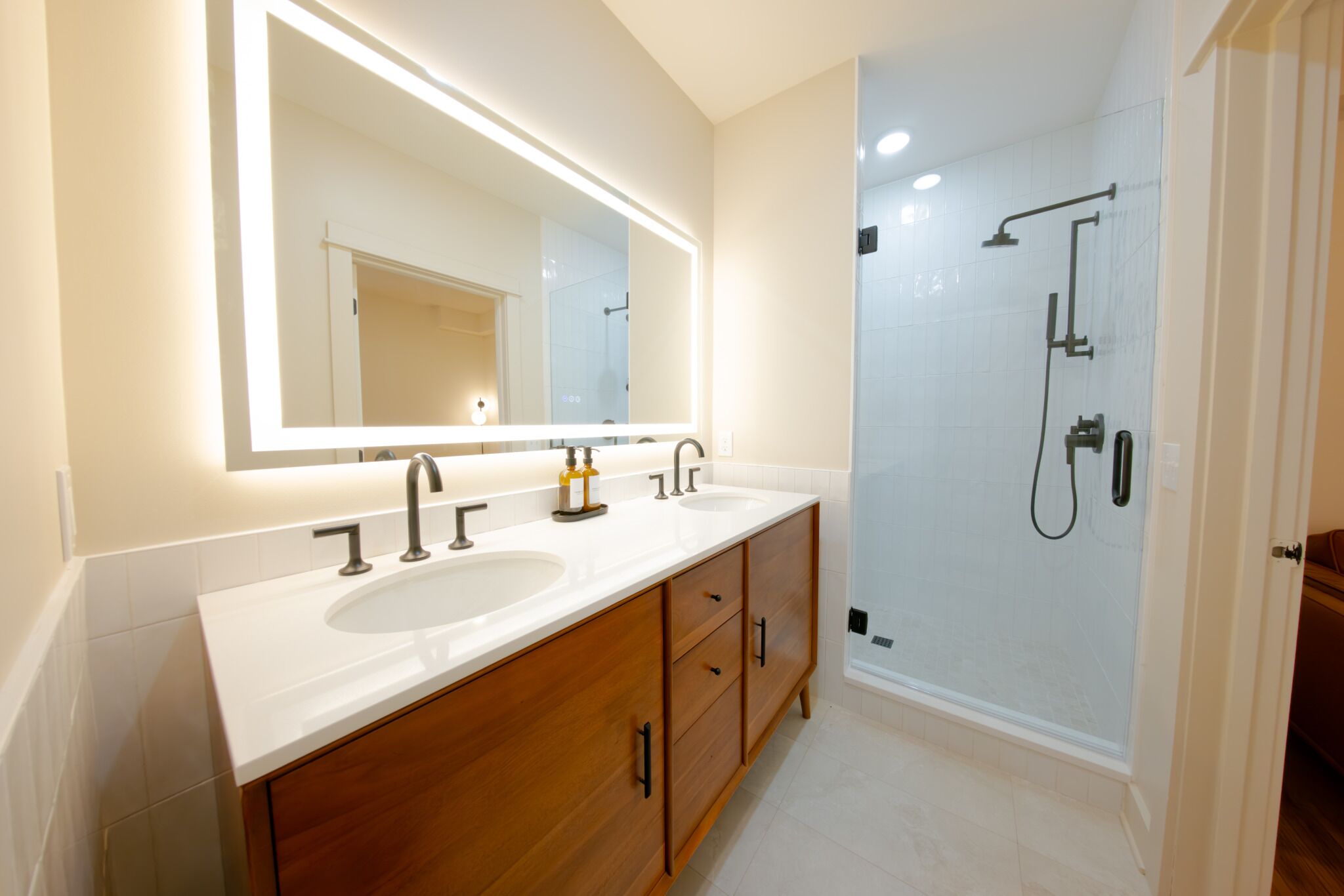 A modern bathroom with a double sink vanity, a large mirror, and a walk-in shower.