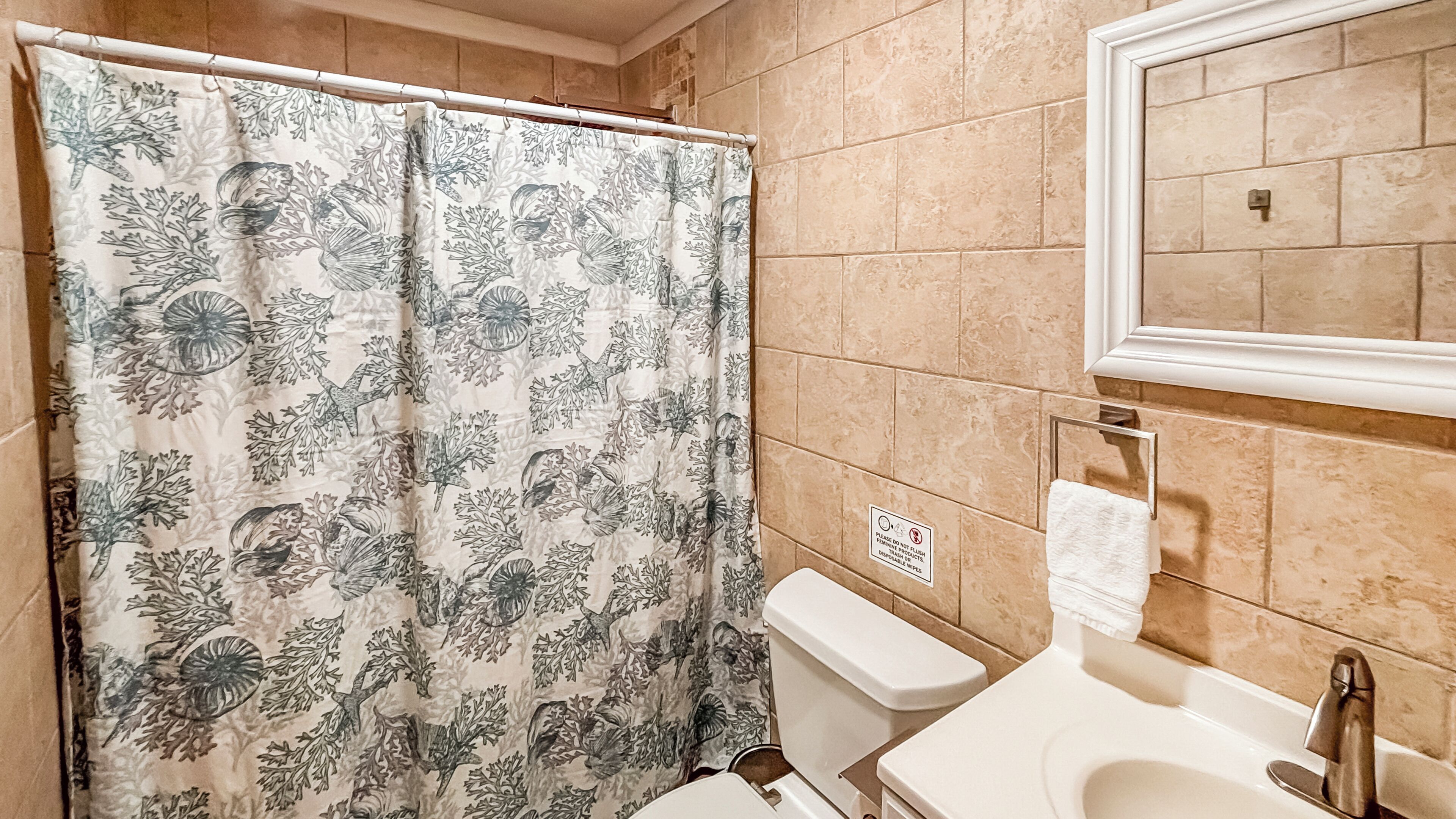A bathroom with a shower curtain featuring a marine life pattern, a toilet, a sink with a faucet, and a mirror above the sink.