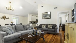 A modern living room with a grey sofa, a wooden coffee table with wine glasses, and a chandelier. - Chic Marigny Retreat Near French Quarter (New Orleans)