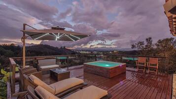Une terrasse en bois avec des chaises longues, un jacuzzi et une balustrade en verre donnant sur un paysage pittoresque.