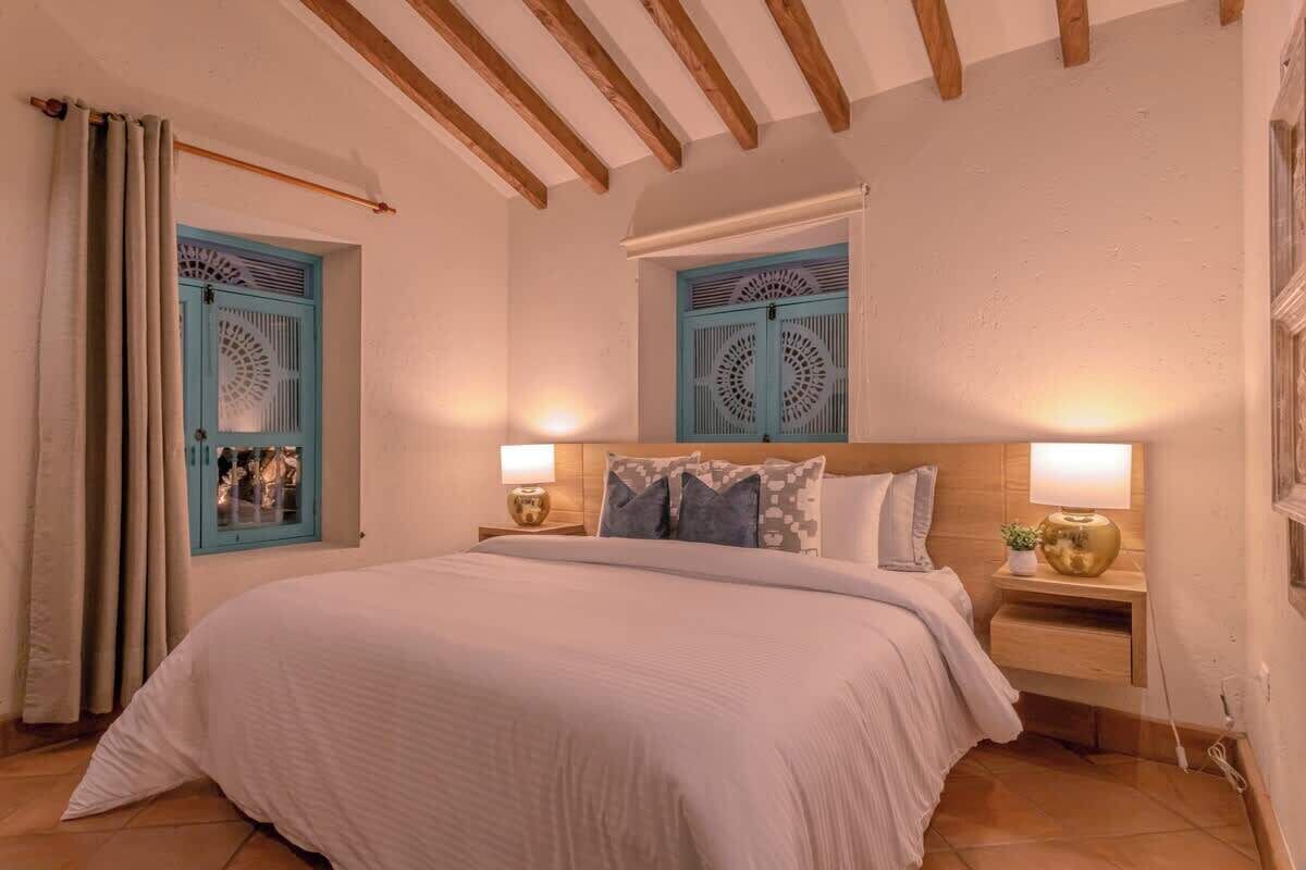 Une chambre à coucher avec un grand lit, deux tables de chevet avec des lampes et deux portes bleues ornées de motifs décoratifs.