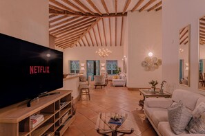 A living room with a large flat-screen TV displaying 'NETFLIX,' a wooden entertainment unit, a glass coffee table, and a sofa.