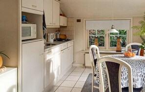 A kitchen with white cabinets, a microwave, a kettle, and a stove. There is a window with a view of greenery outside.