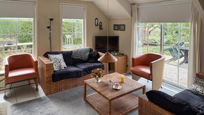 A spacious living room with a sofa, two armchairs, a coffee table, and a television. Large windows offer views of a garden. - Cozy home in Ermelo with WiFi (Ermelo)