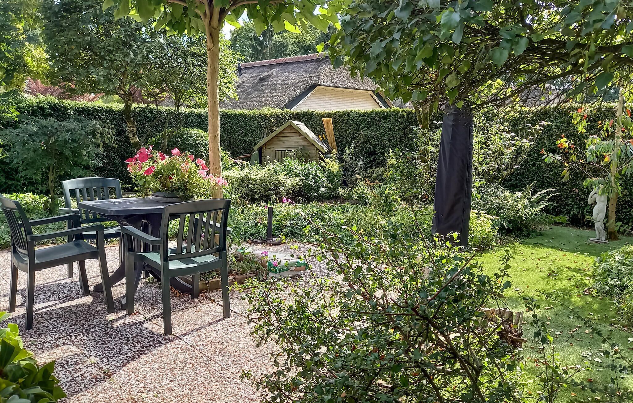 A garden with a table and chairs, a thatched-roof building, and various plants.