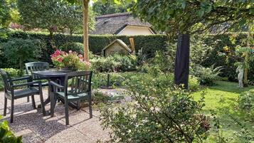 A garden with a table and chairs, a thatched-roof building, and various plants.