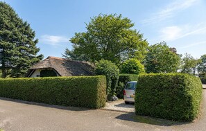 A house with a thatched roof, surrounded by well-maintained hedges and trees.