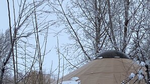 Una yurta con puerta de madera, rodeada de árboles cubiertos de nieve.
