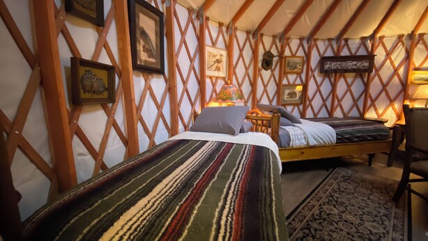 Una habitación acogedora con una cama, una silla y una mesita. Hay cuadros enmarcados en la pared y una lámpara sobre la mesa.
