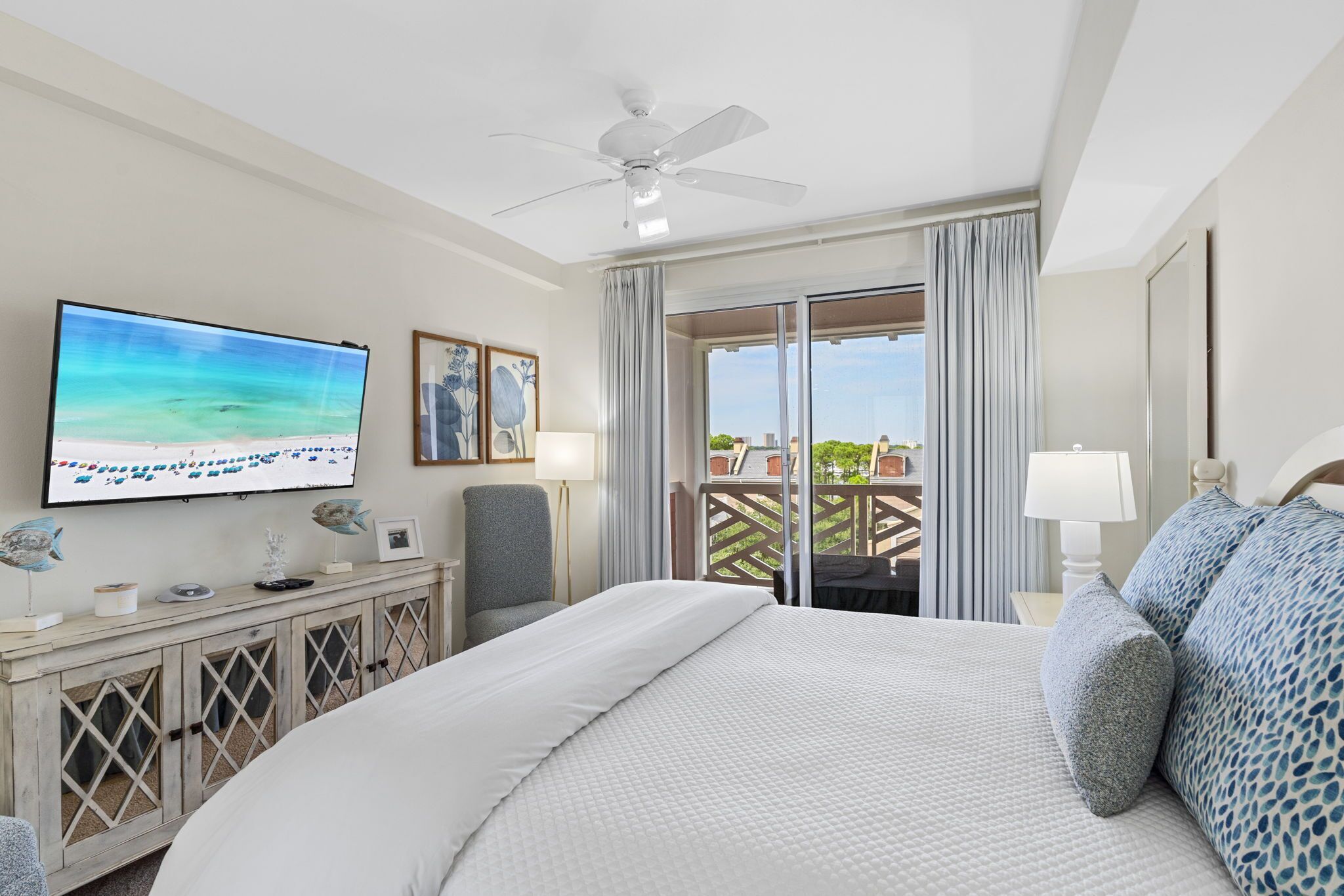 Une chambre d’hôtel équipée d’un lit, d’une télévision, d’un ventilateur de plafond, d’un balcon avec vue et d’un bureau avec une lampe.