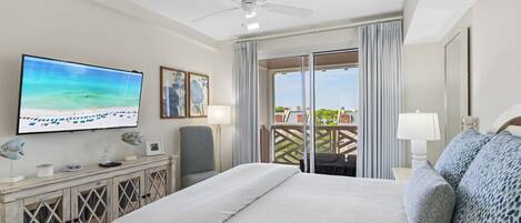 Une chambre d’hôtel équipée d’un lit, d’une télévision, d’un ventilateur de plafond, d’un balcon avec vue et d’un bureau avec une lampe.
