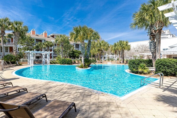 A swimming pool with lounge chairs, palm trees, and a building with a white facade.