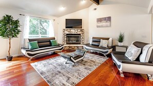 A modern living room with a stone fireplace, leather sofas, a glass coffee table, and a large potted plant. - Yosemite + Bass Lake – Hot Tub, Games, Sleeps 13 (Oakhurst)