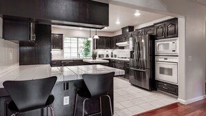 A modern kitchen with dark cabinetry, stainless steel appliances, and a central island with bar stools. - Yosemite + Bass Lake – Hot Tub, Games, Sleeps 13 (Oakhurst)