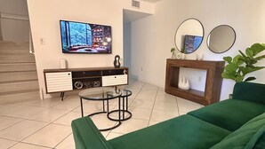 A living room with a green sofa, a TV on the wall, a small table, and a plant. - Beautiful 2/2.5 Condo w/free parking fast WiFi (Miami)
