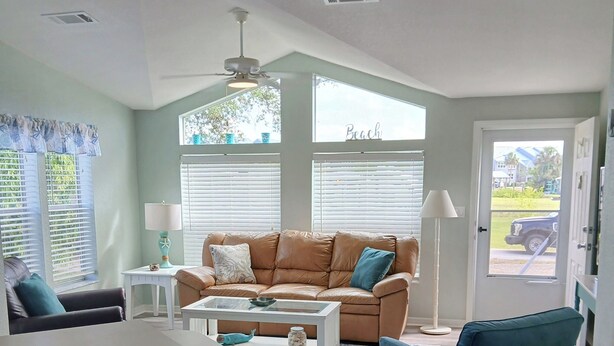 A modern living room with a brown leather sofa, a blue armchair, a white coffee table, and a kitchen area with a bar counter.